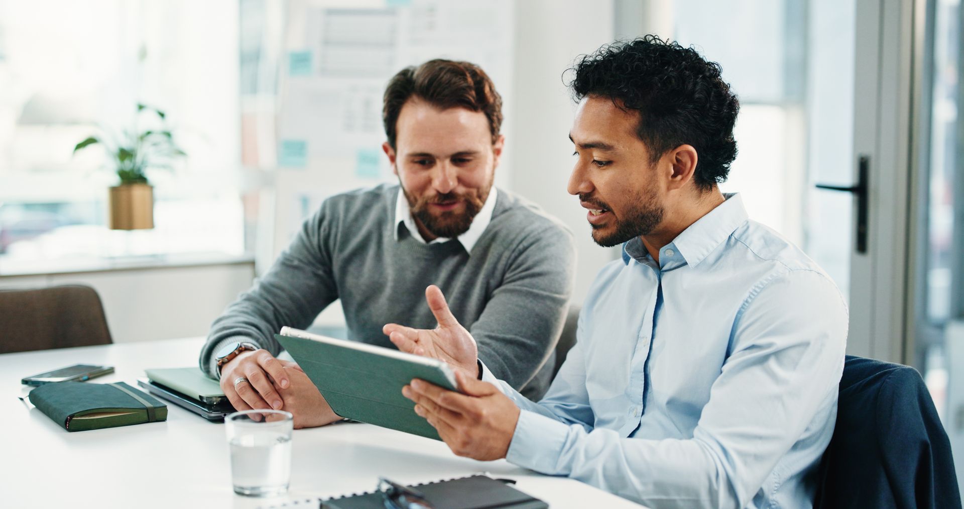 Two business professionals review information on a tablet while meeting at a desk in a modern office
