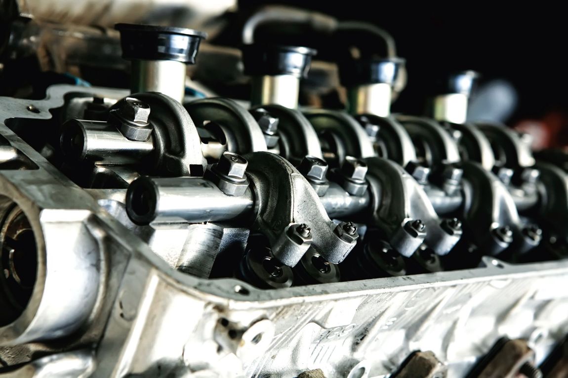 Engine's cylinder head with rocker arms, nuts, and bolts visible, in a mechanical setting.