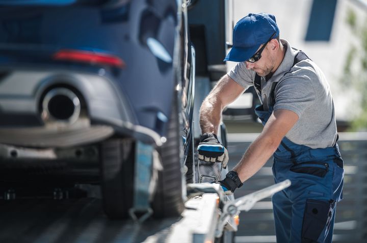 A tow truck operator securing a blue car on a flatbed.