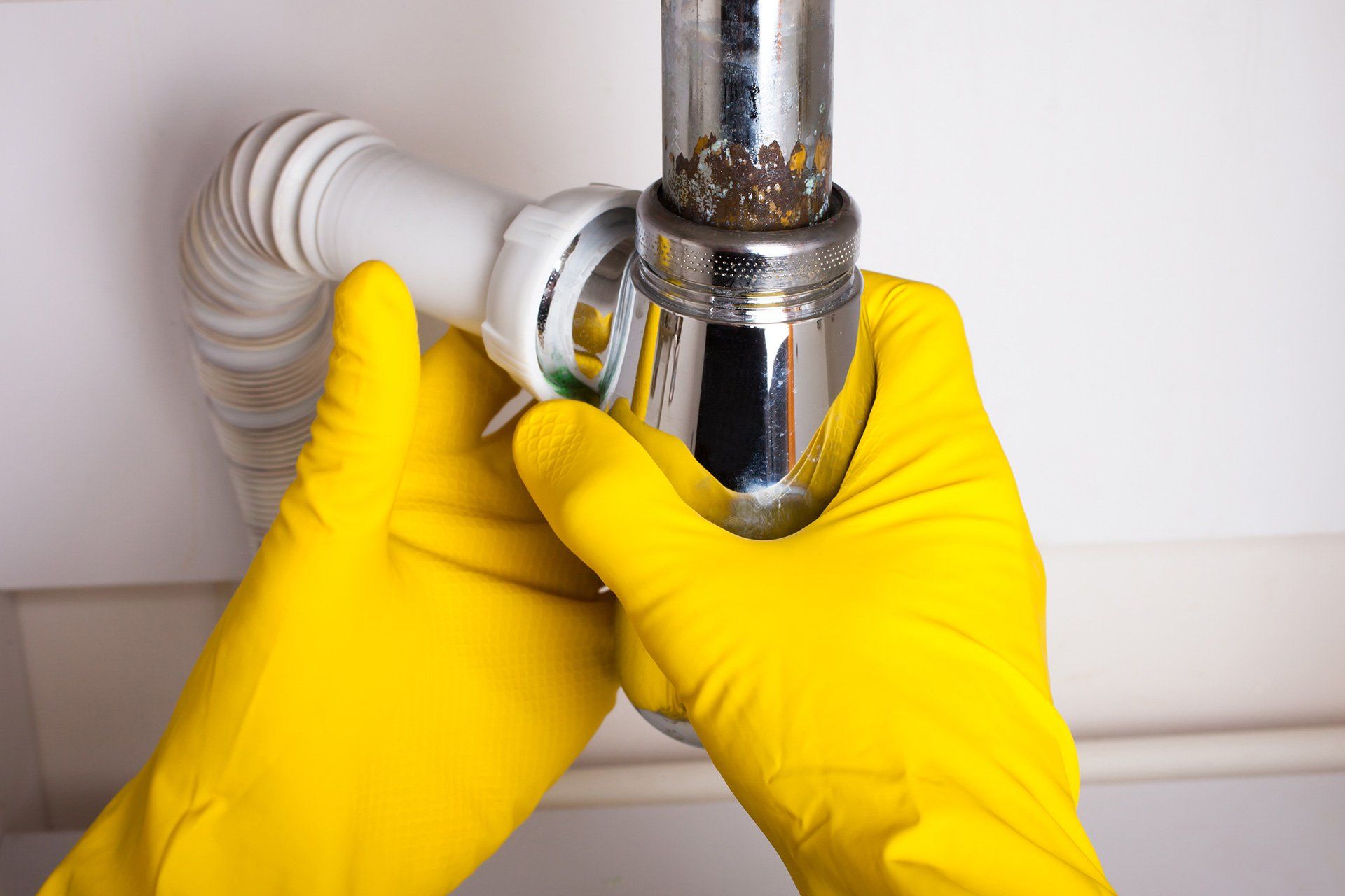 A person wearing yellow gloves is fixing a sink pipe.