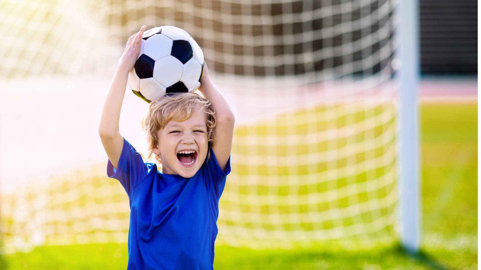 a young boy is holding a soccer ball over his head .