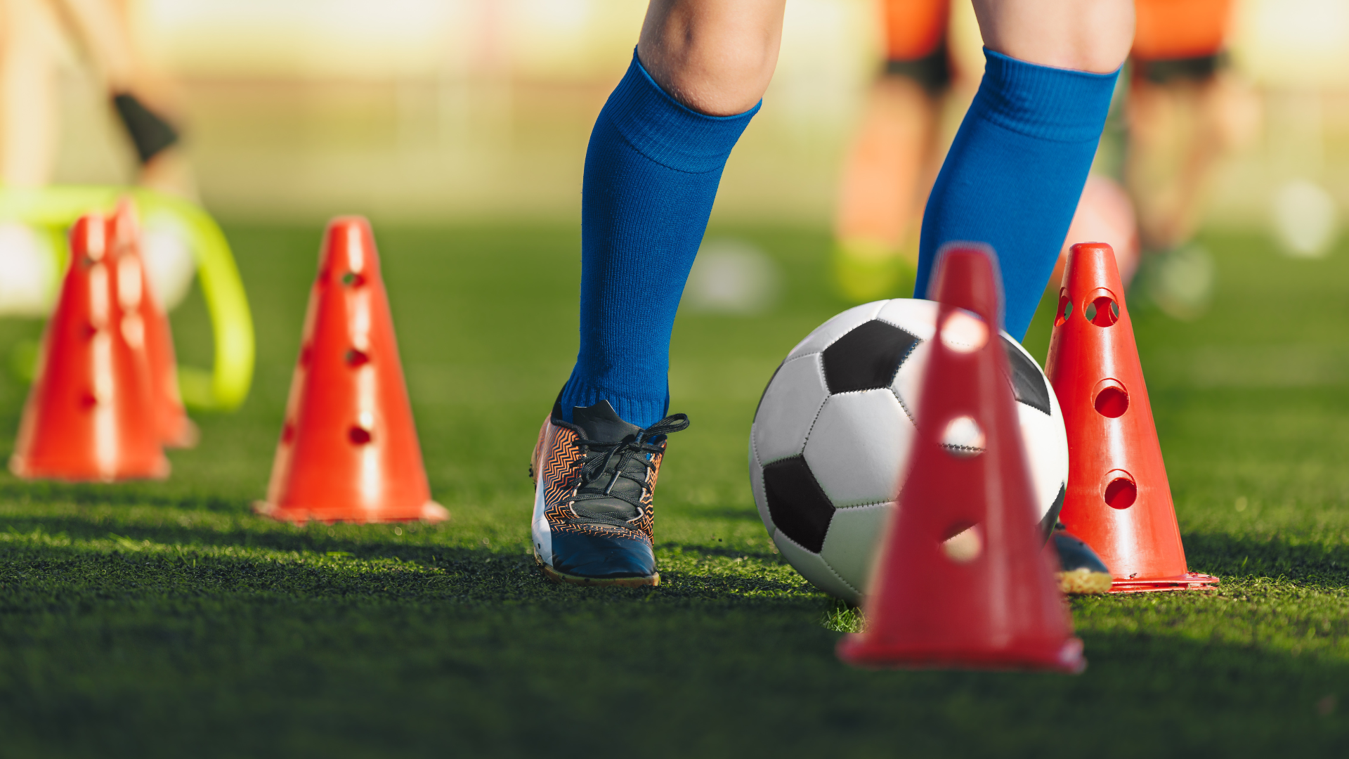 a soccer player is kicking a soccer ball between cones on a field .