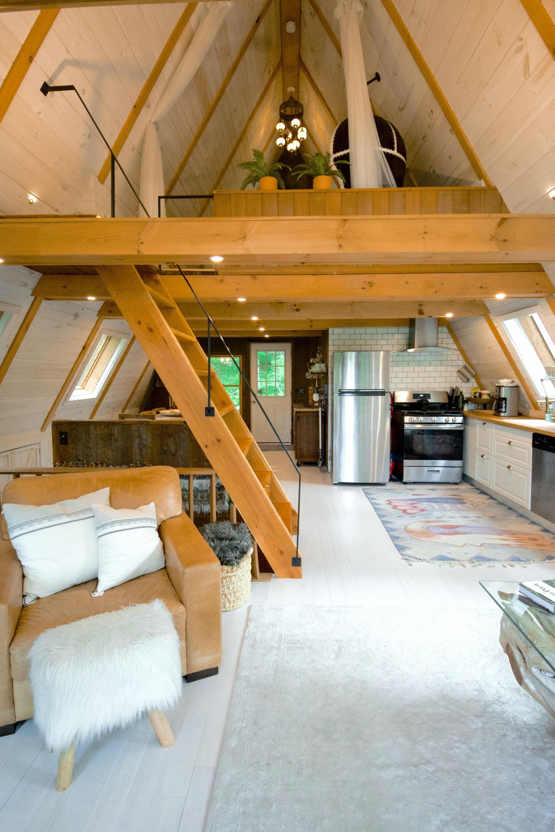 Cozy A-frame cabin interior with loft, leather chair, wooden ladder, and modern kitchen.