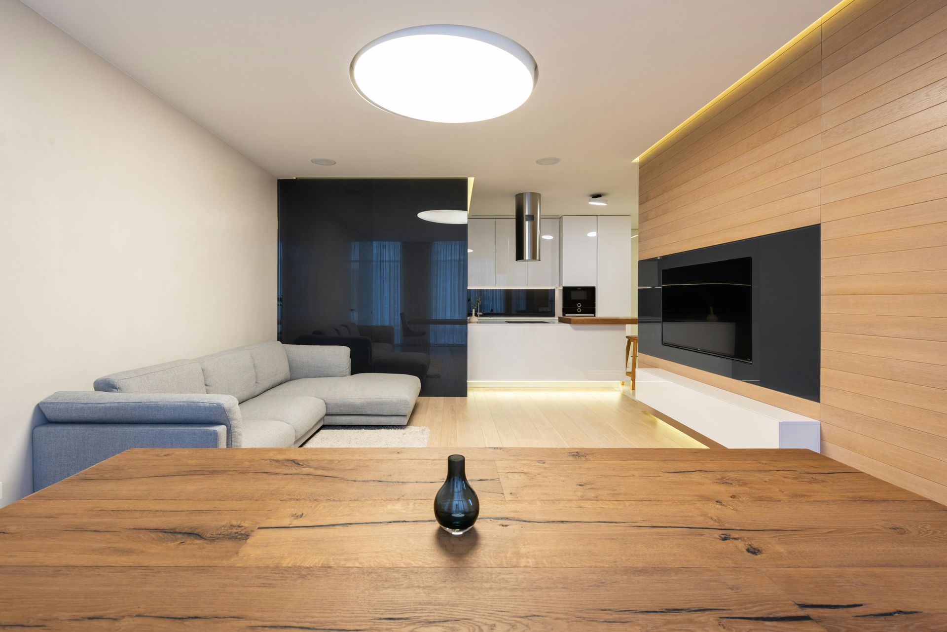 Modern living room with light wood paneling, gray sofa, and a table in the foreground.