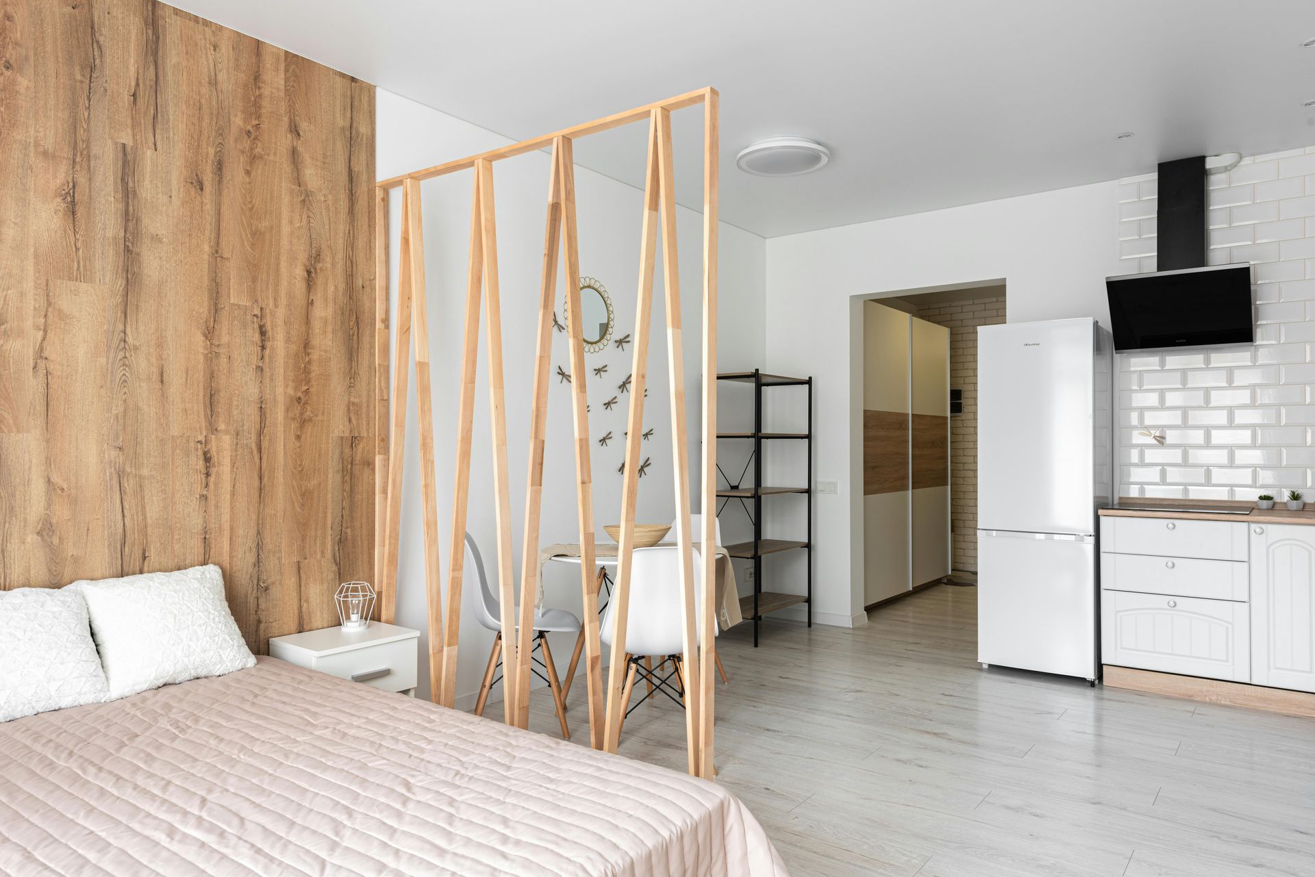 Small studio apartment with wooden accents, bed, kitchen, and decorative divider.