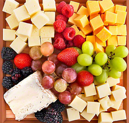 A wooden tray filled with cheese grapes strawberries raspberries and blackberries
