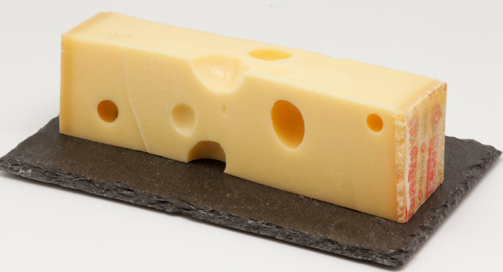 A piece of cheese with holes in it is on a slate tray