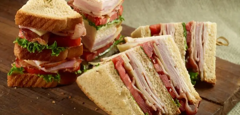 Three club sandwiches are stacked on top of each other on a wooden cutting board.