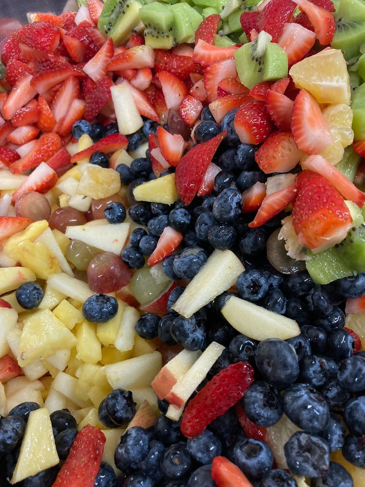 A close up of a fruit salad with strawberries blueberries apples and kiwi