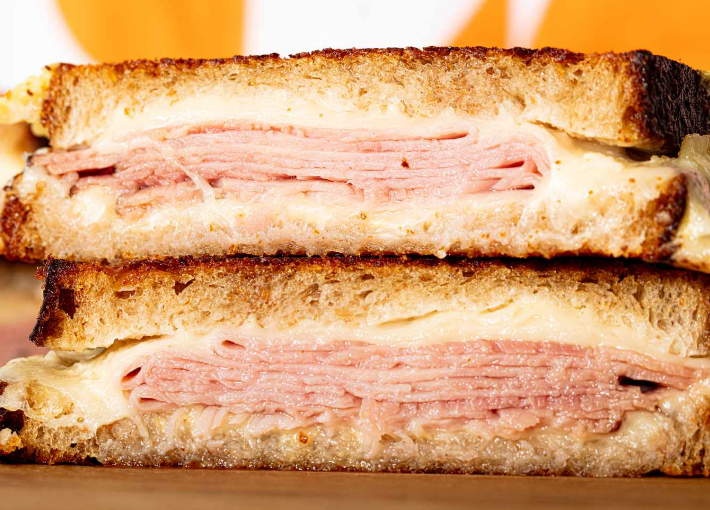 A grilled ham and cheese sandwich is cut in half on a wooden table.