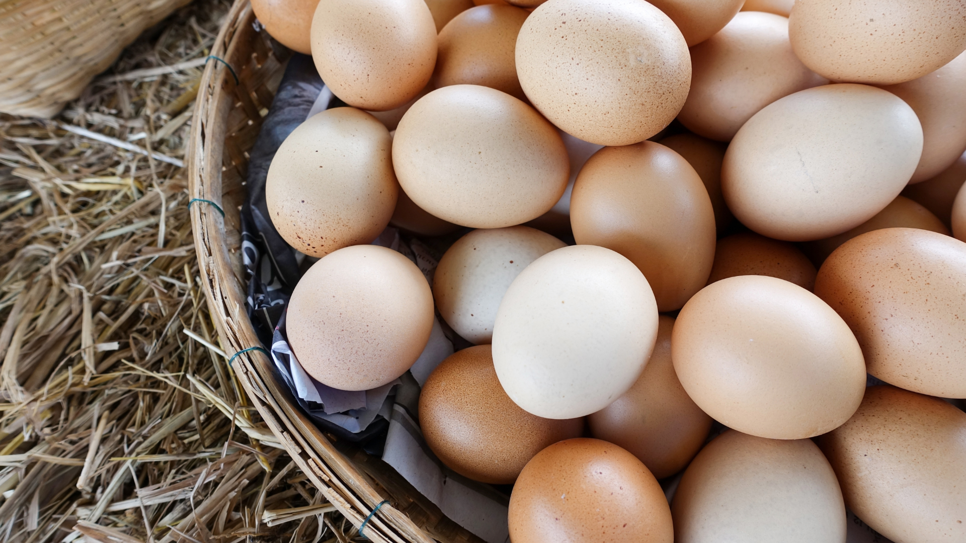 A basket filled with eggs is sitting on a pile of hay.