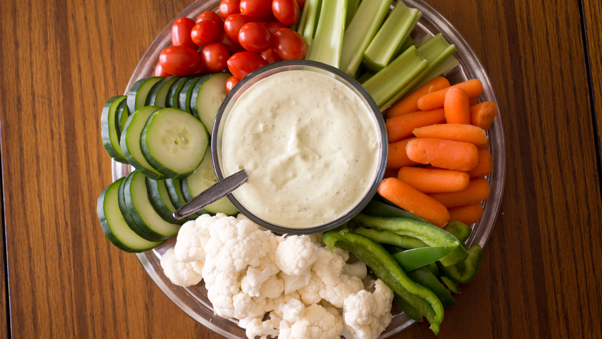 A plate of vegetables and dip on a wooden table.