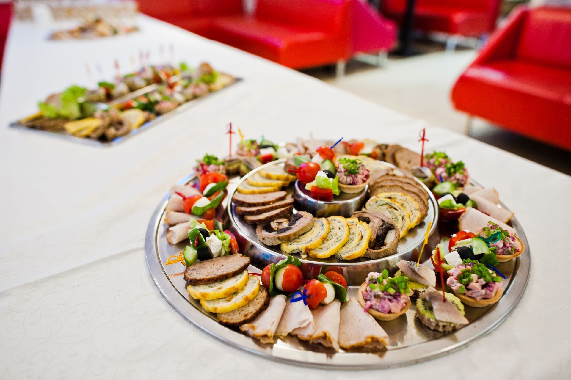 Buffet platter with assorted meats and appetizers on a table, with red seating in the background.