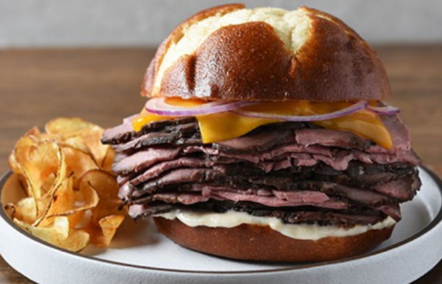 A sandwich with a pretzel bun and chips on a plate.
