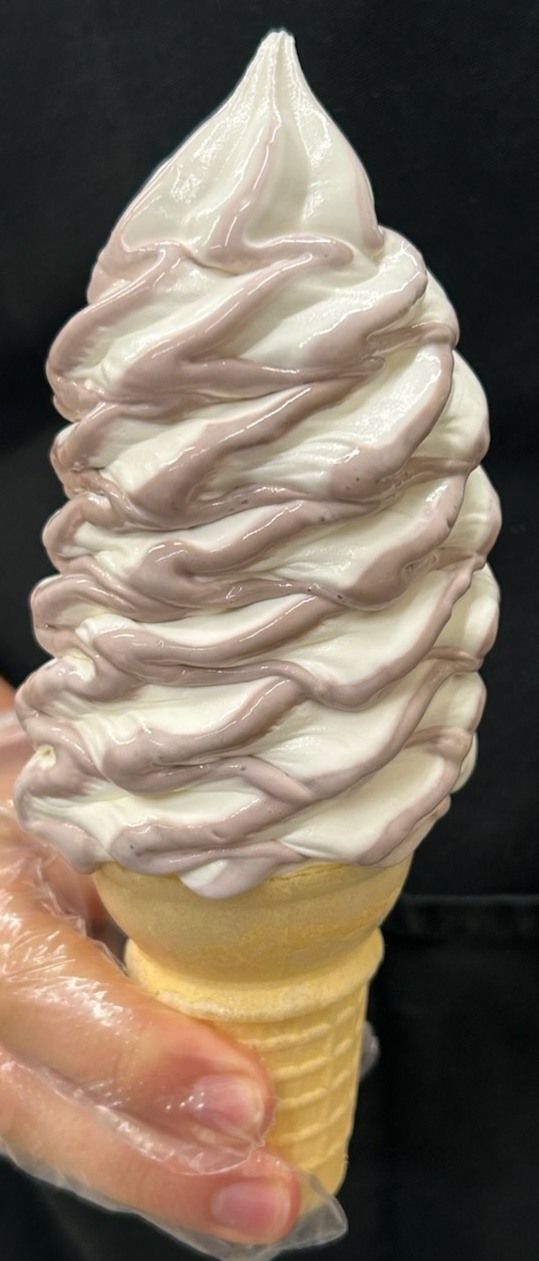 Soft serve ice cream cone drizzled with a purple sauce held in a gloved hand.