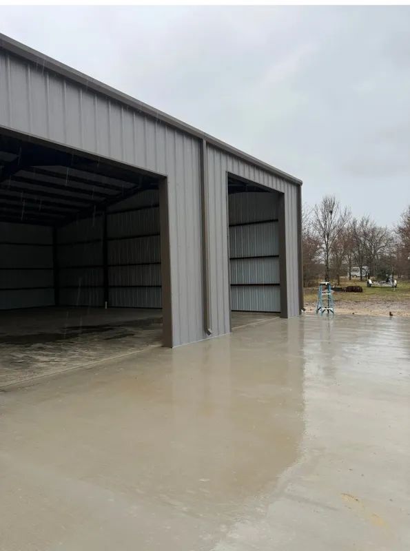 Large gray metal warehouse with open bays on a flooded concrete lot