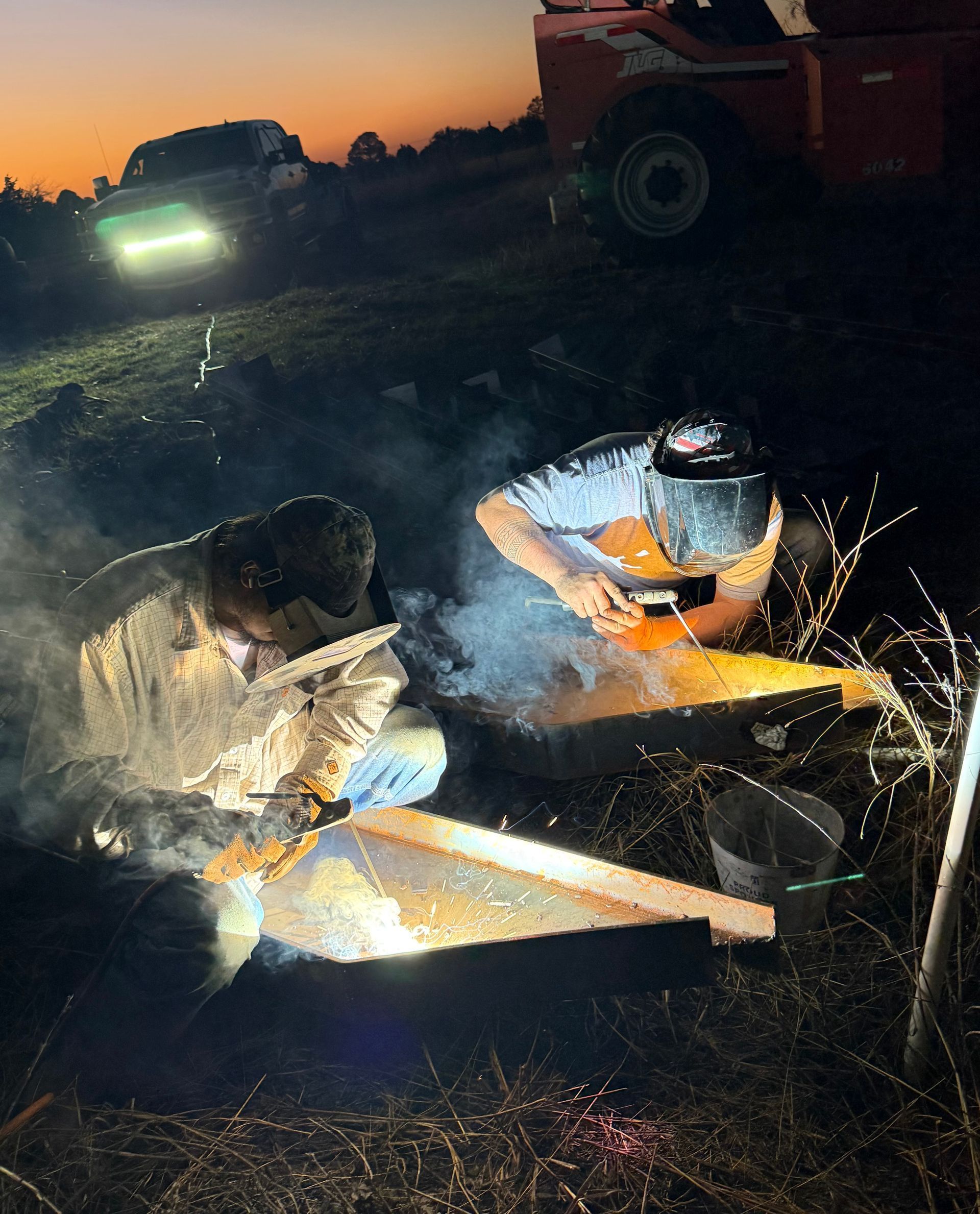 Worker in reflective gear welding metal at dusk beside heavy machinery, sparks flying.