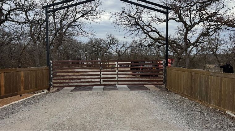 Gravel driveway leading to a wooden gate and fence under bare trees on an overcast day