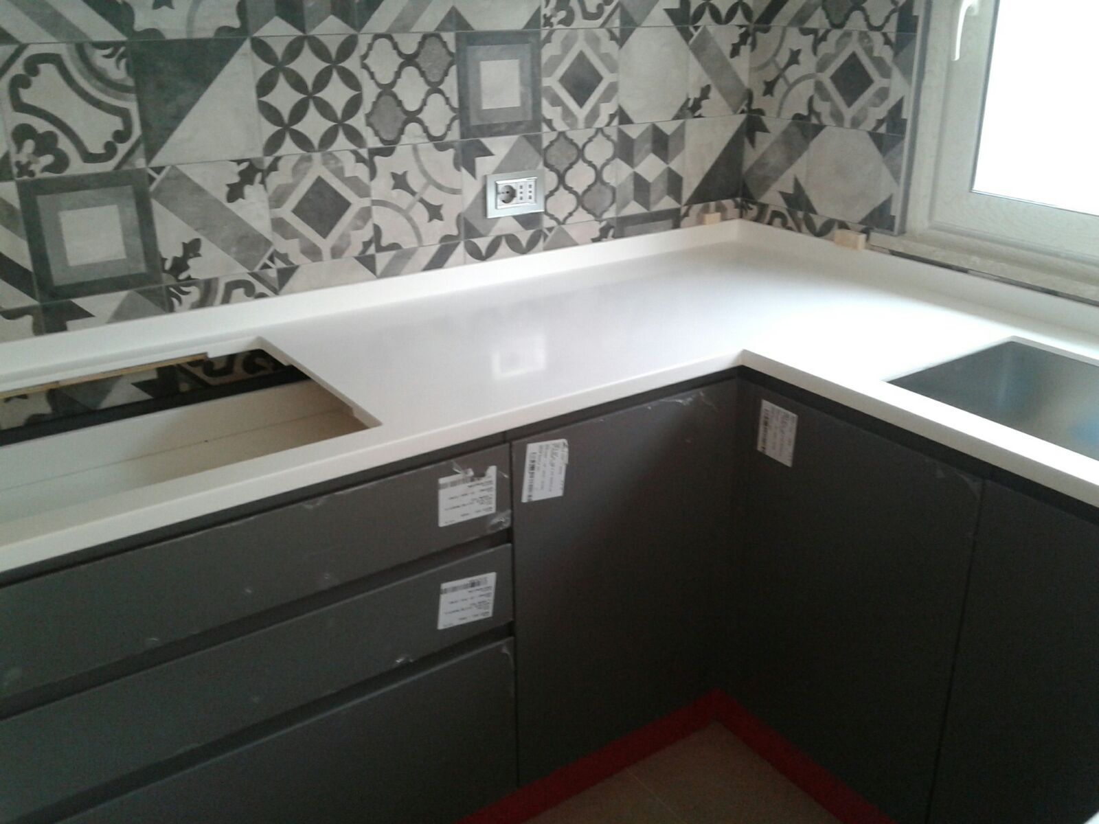 Cucina con piano di lavoro bianco e mobili grigi, paraschizzi decorato, lavello.