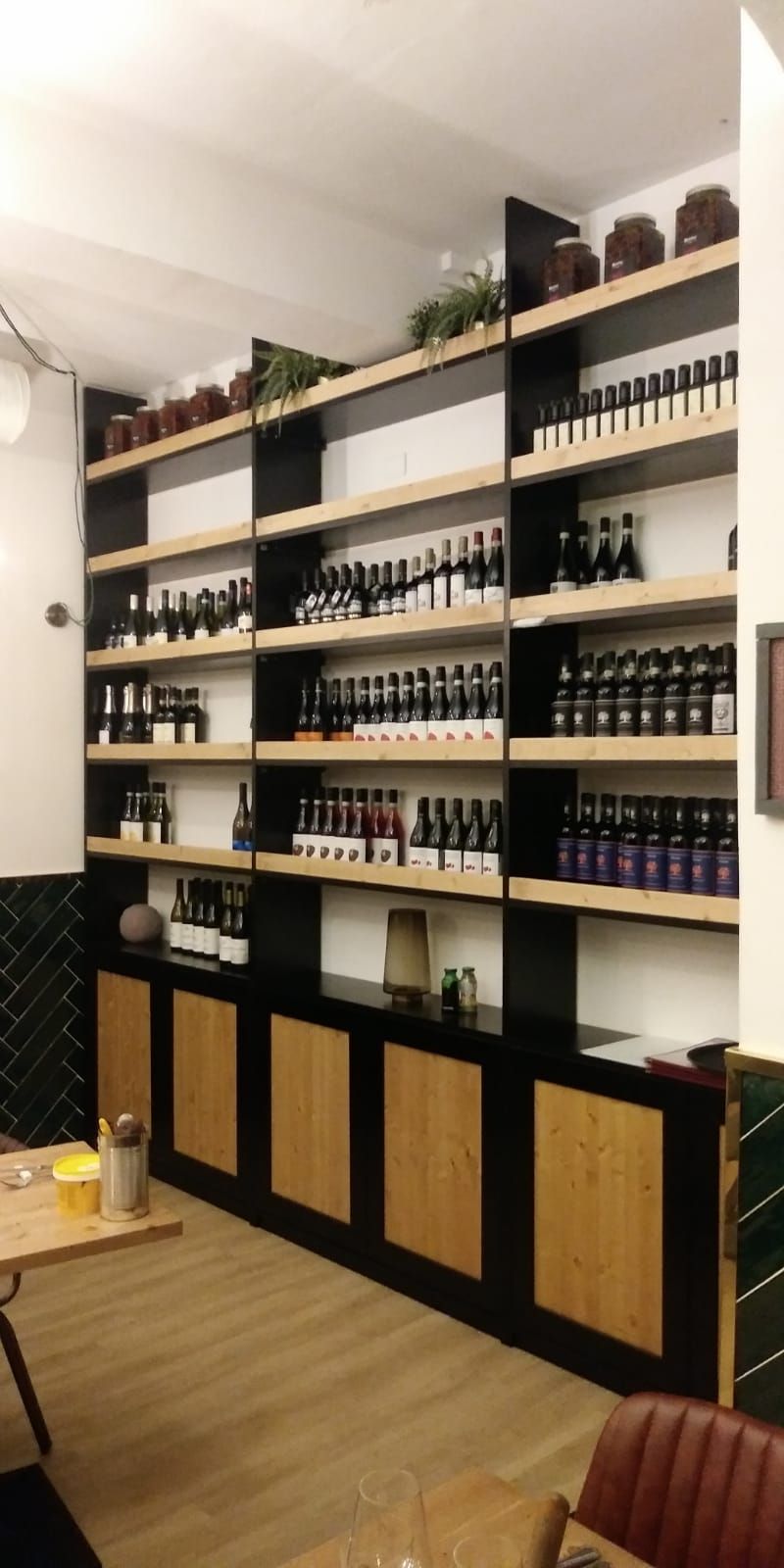 Scaffali pieni di bottiglie di vino in un negozio. Sotto ci sono armadietti in legno e il pavimento è chiaro.