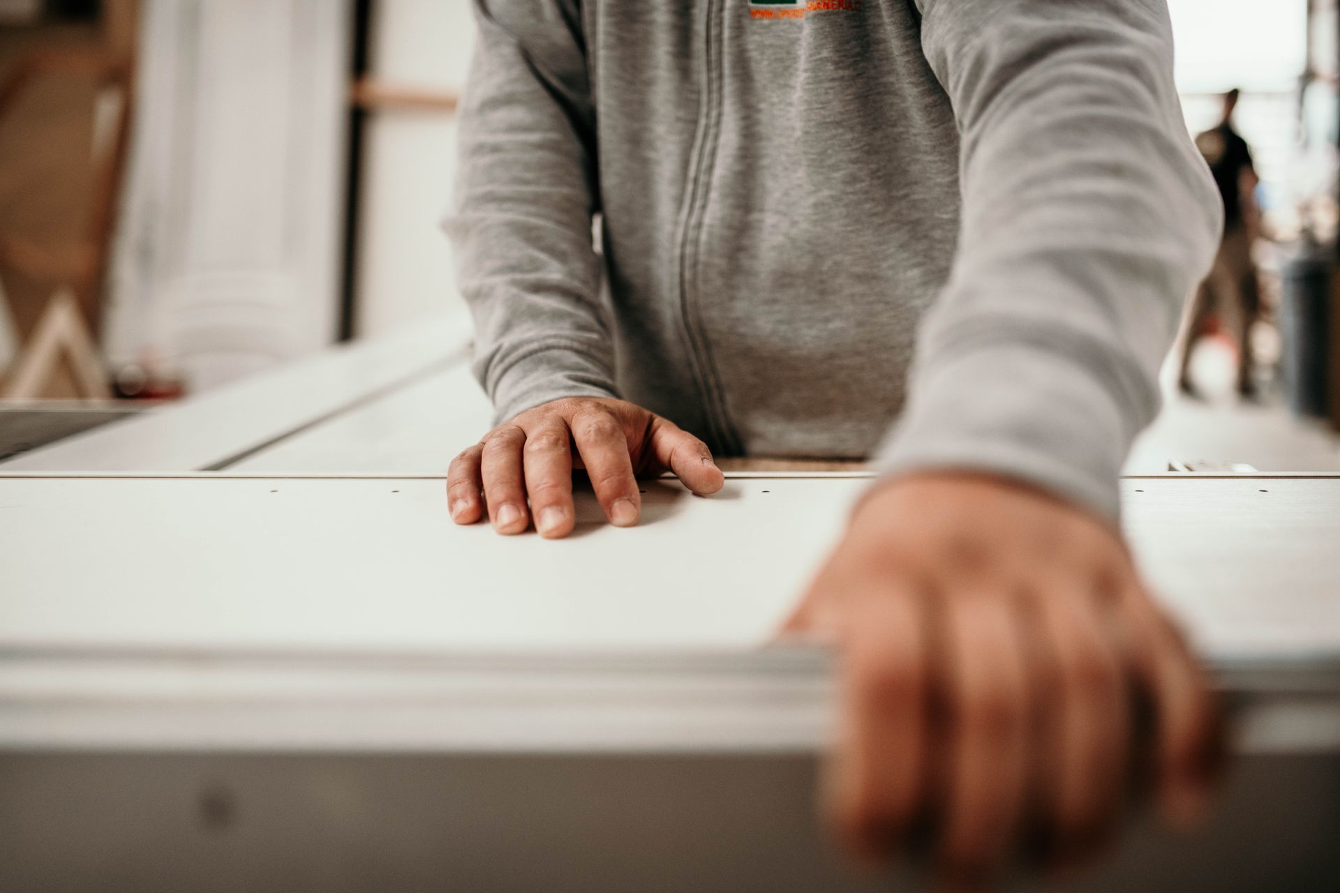 Mani di una persona su una superficie chiara in un'officina, con indosso una felpa grigia.