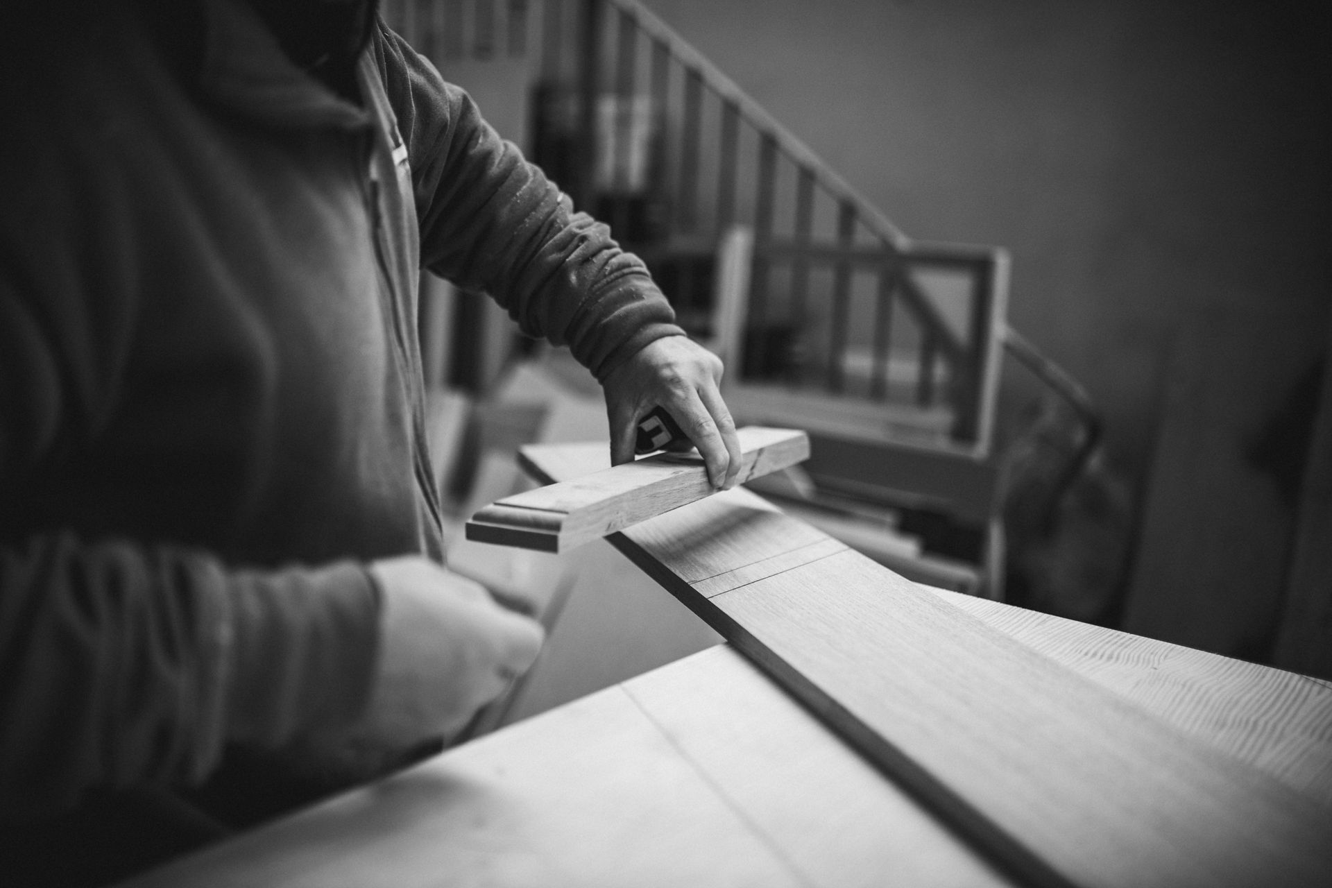 Persona che leviga il legno in un laboratorio. Bianco e nero, incentrato sulle mani e sul legno.