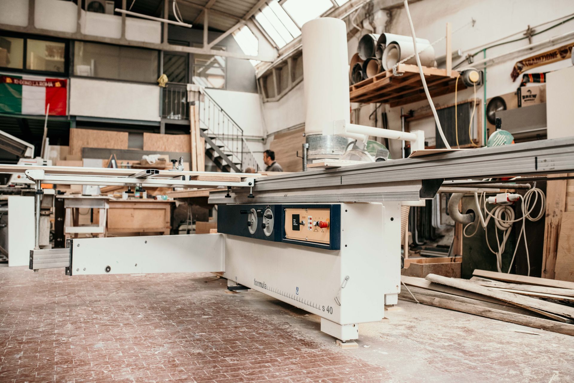 Un laboratorio di falegnameria con una grande segatrice; segatura sul pavimento.