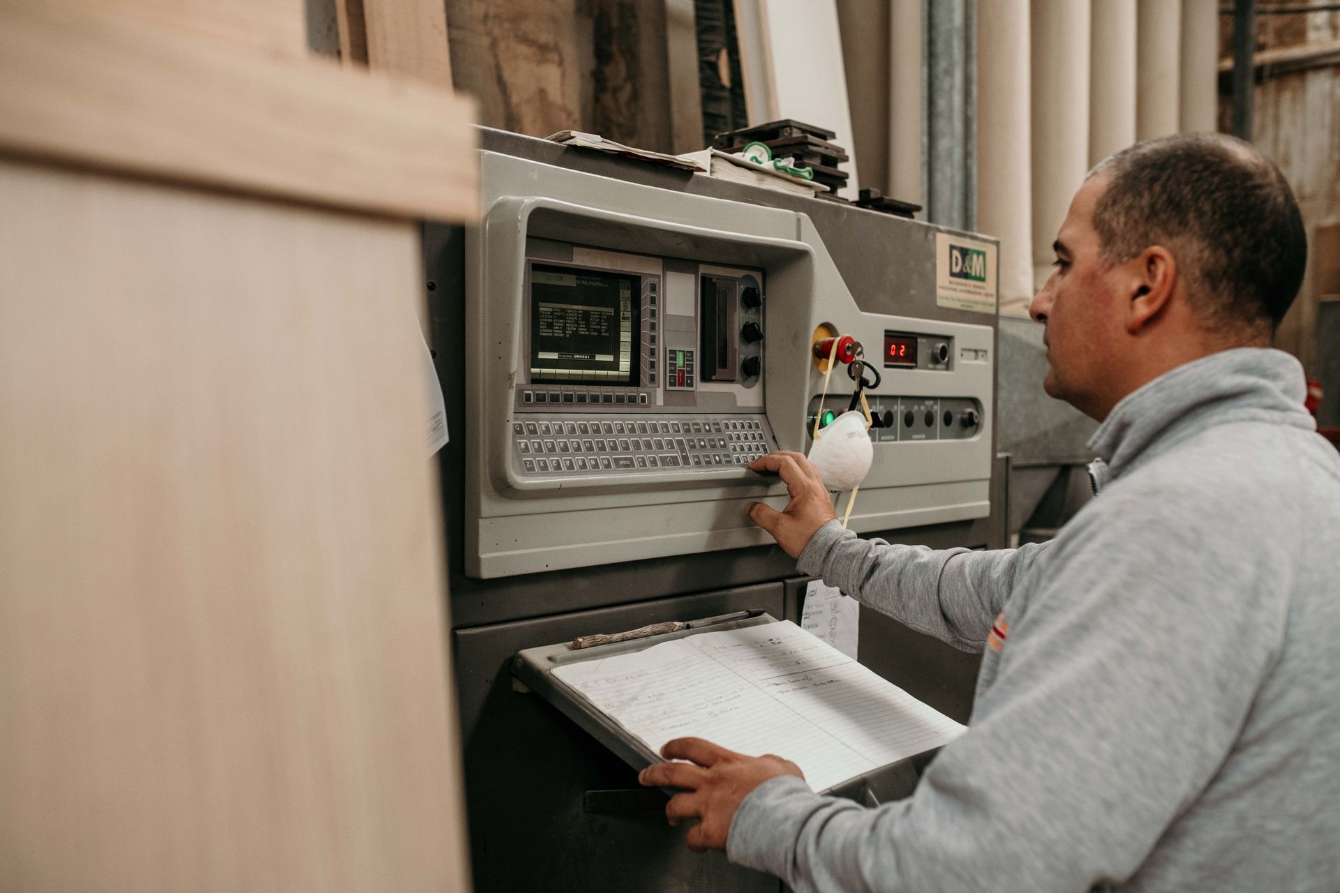 Uomo che aziona una macchina CNC in una falegnameria, utilizzando tastiera e comandi.