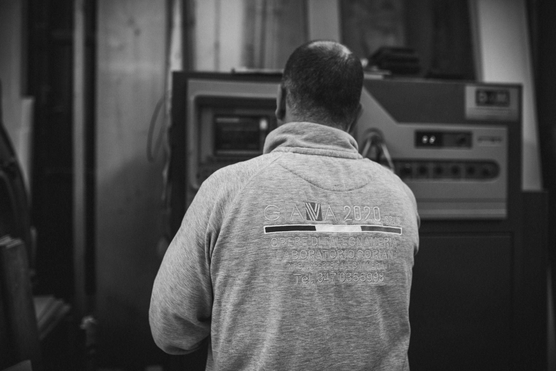 Uomo con felpa grigia che aziona macchinari in un'officina.