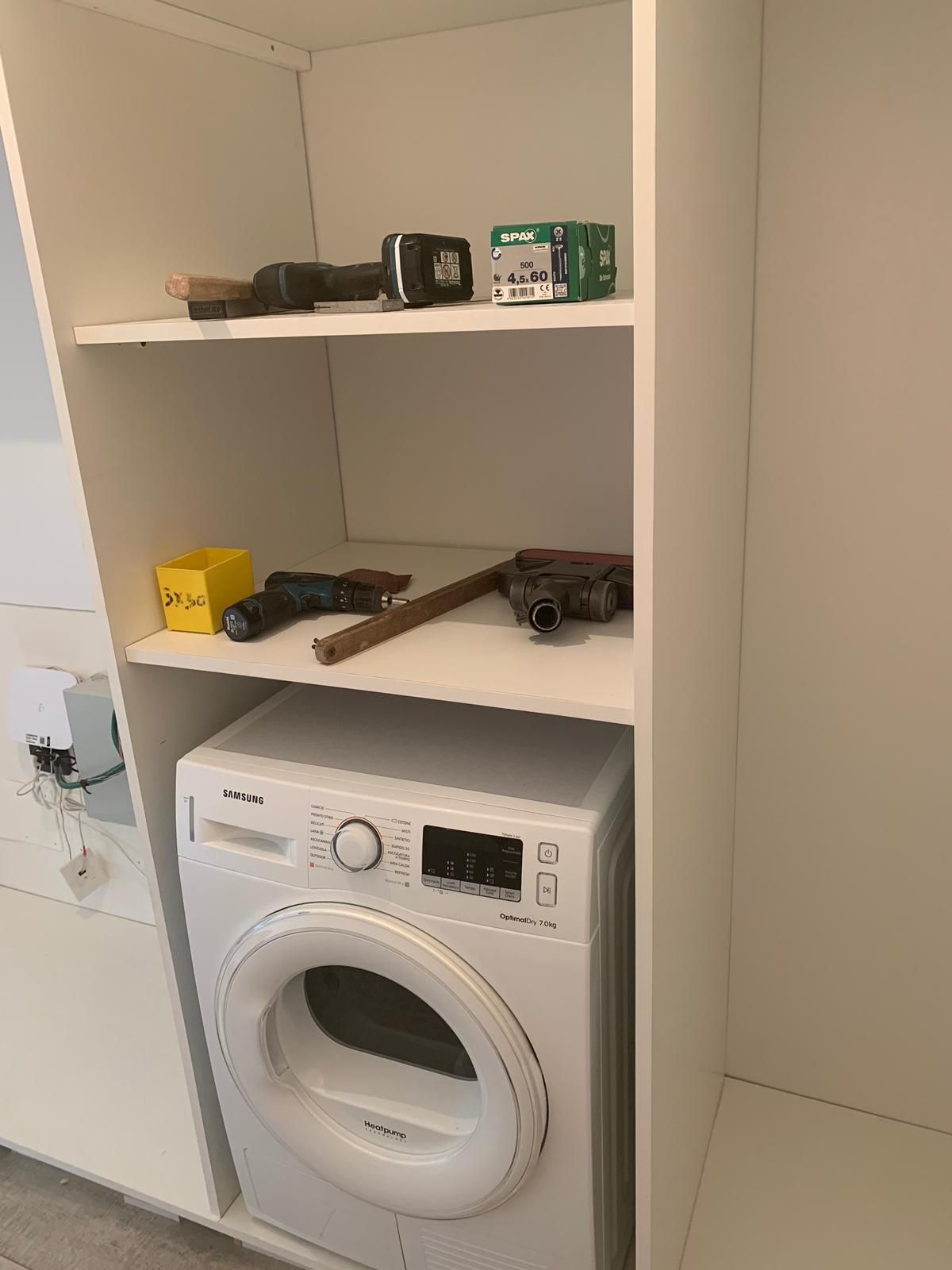Mobile bianco con lavatrice in basso e ripiani con attrezzi.