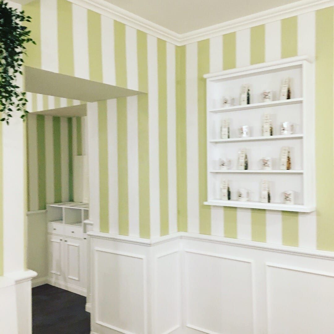 Pareti a strisce verdi e bianche con finiture bianche, uno scaffale con oggetti in esposizione e una porta.