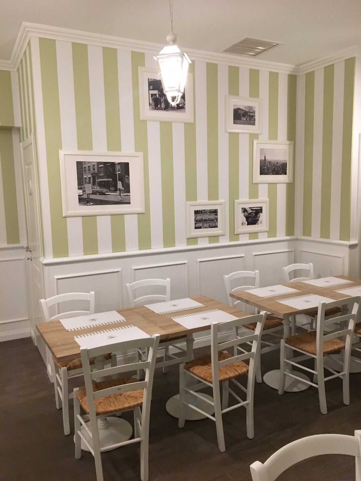 Interno del ristorante: tavoli e sedie con carta da parati a righe verde chiaro, foto incorniciate e una lampada sospesa.