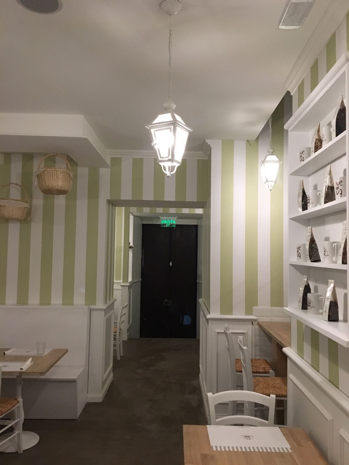 Interno di un ristorante con pareti a strisce verdi e bianche, scaffali pieni di prodotti e lanterne bianche appese.