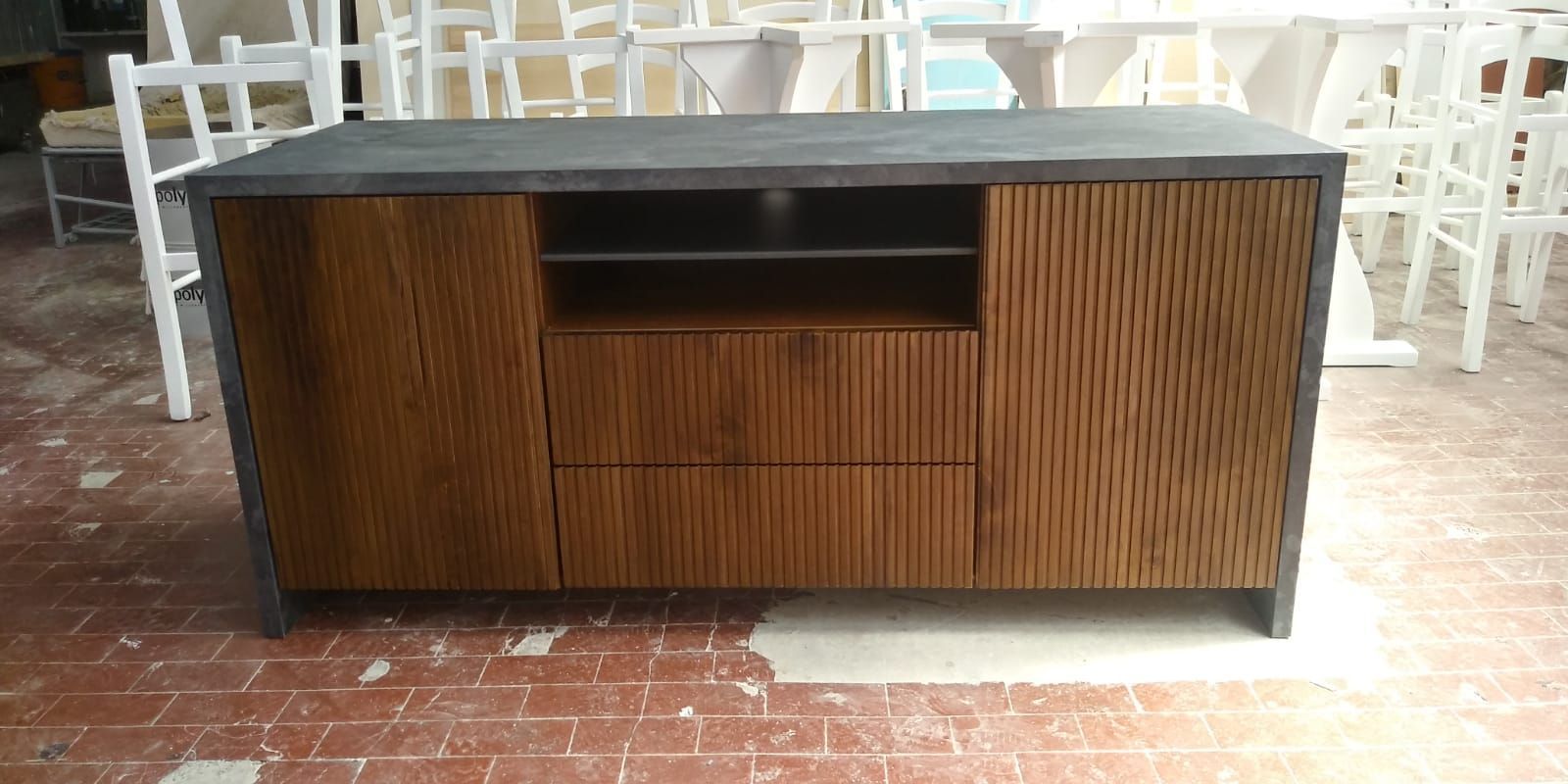 Un mobile in legno con piano grigio e ante e cassetti decorati con scanalature. Sedie bianche sullo sfondo.