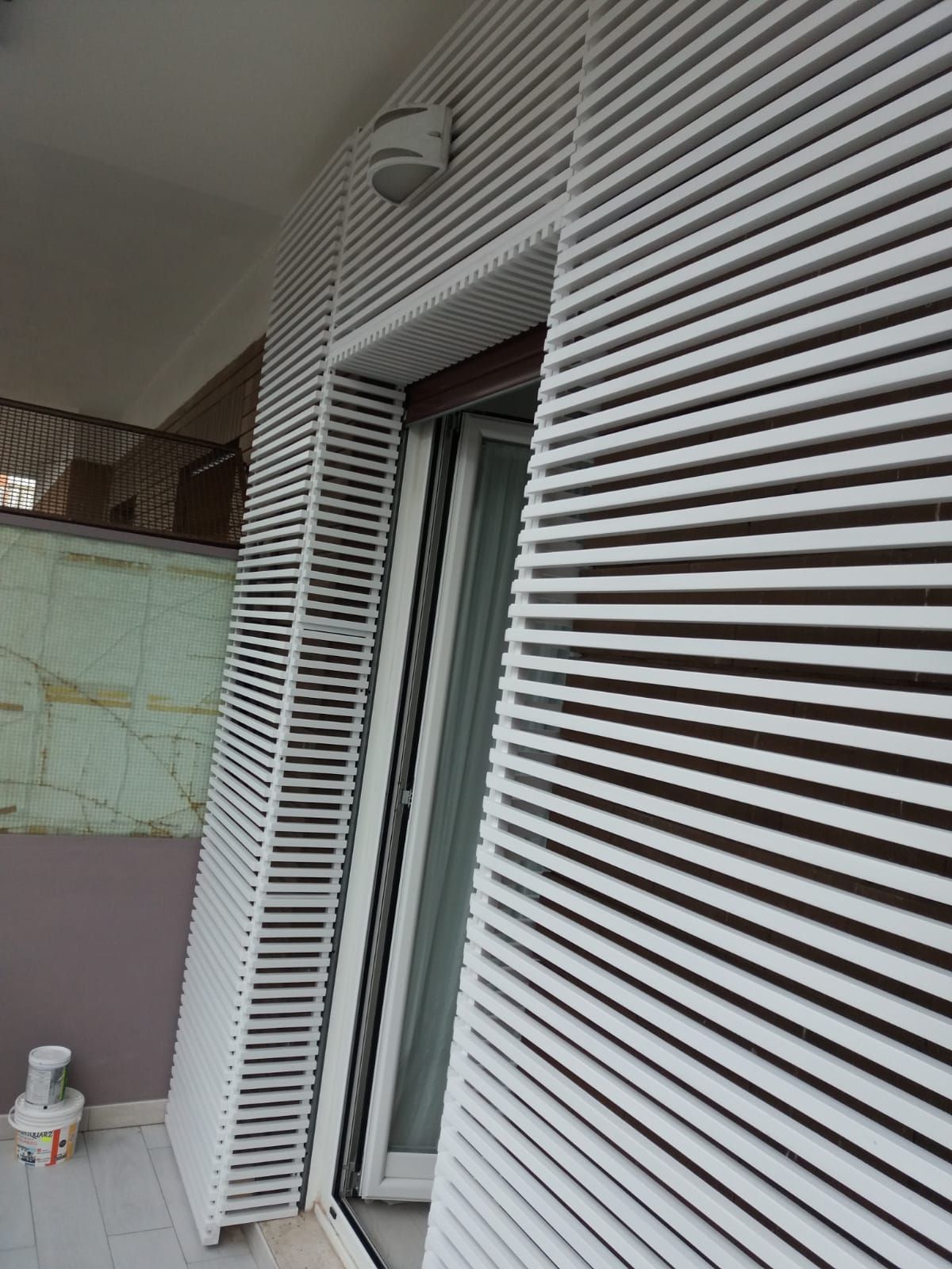 Tende da sole bianche a stecche accanto a una porta a vetri su un balcone.