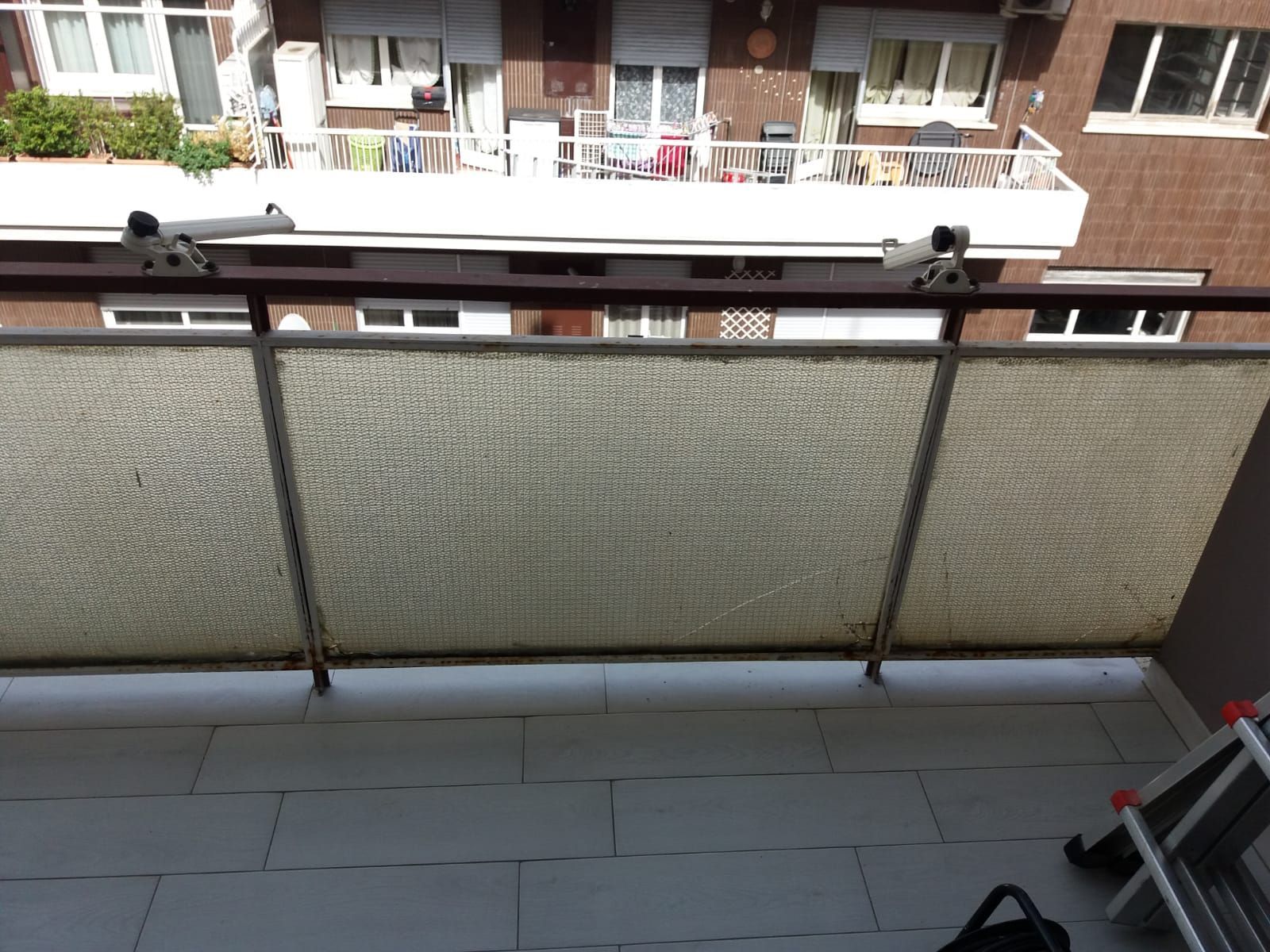 Balcone con pannelli in vetro smerigliato e ringhiera in metallo, con vista sugli edifici sullo sfondo.