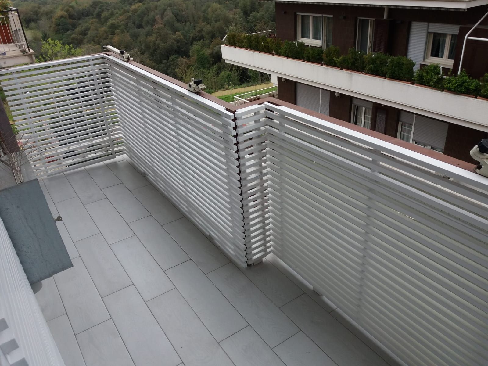 Balcone con schermi bianchi per la privacy, pavimento grigio chiaro e un edificio sullo sfondo.
