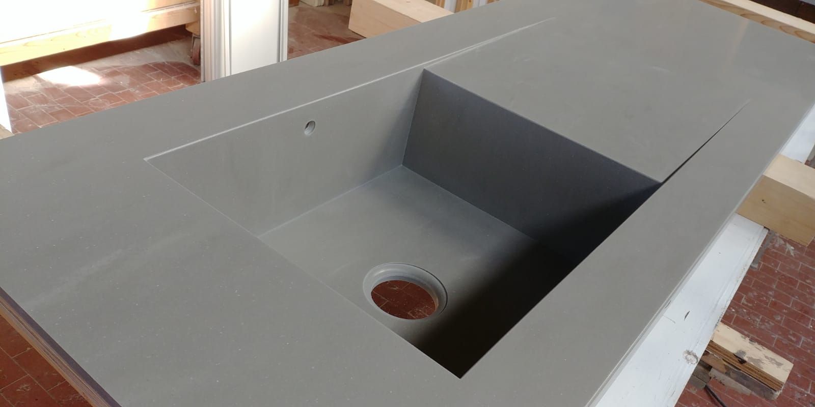 Un piano di lavoro in cemento grigio con un lavello rettangolare incorporato. Il lavello ha un foro di scarico e il piano di lavoro si trova in un'officina.