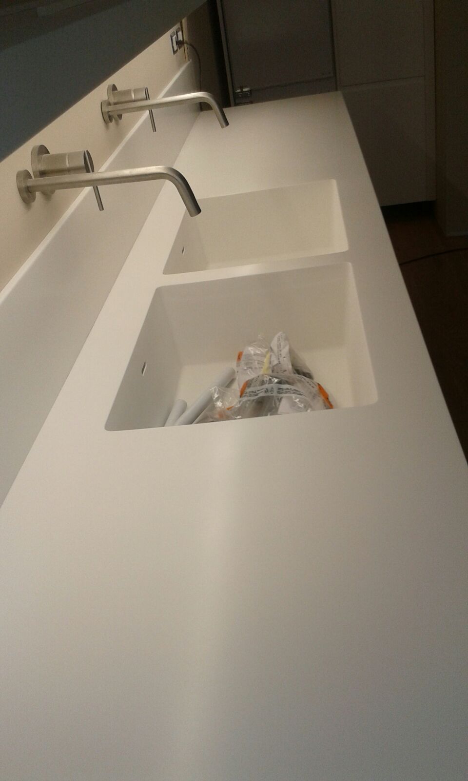 Piano di lavoro bianco con ripiani integrati, rubinetti cromati a parete.