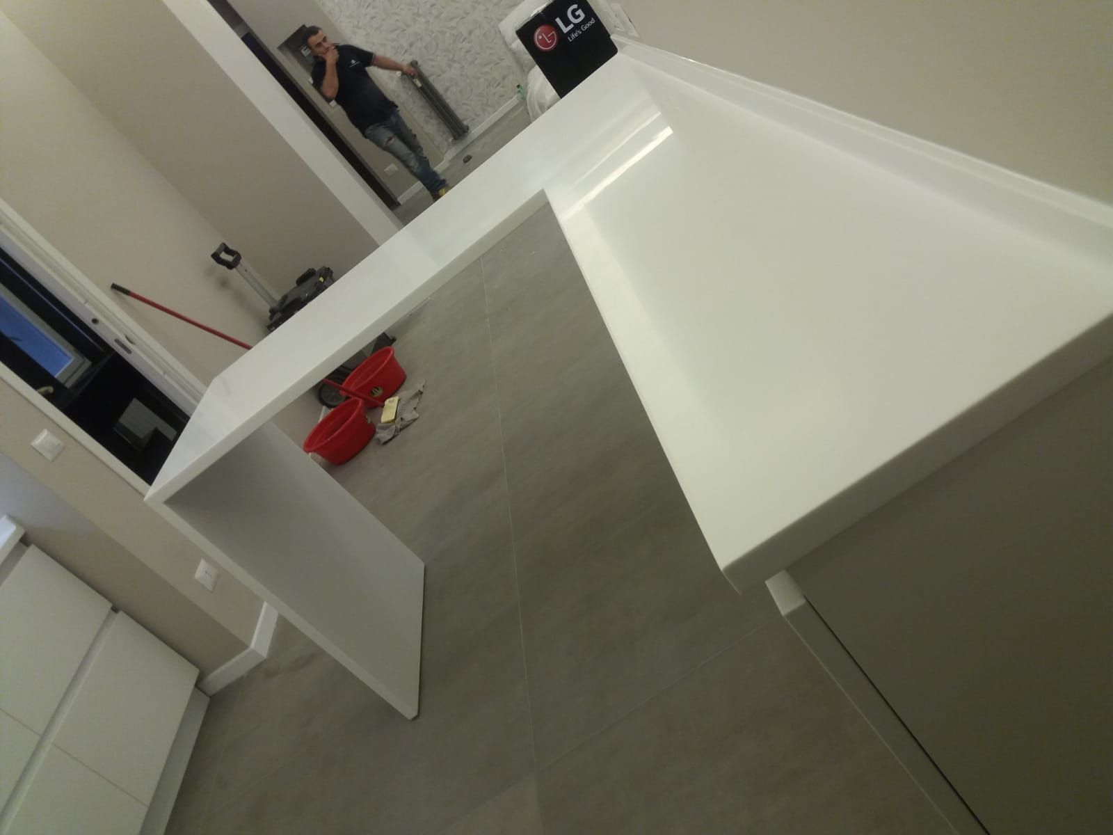 Piano di lavoro bianco con scrivania integrata e mobili contenitori in una cucina moderna.