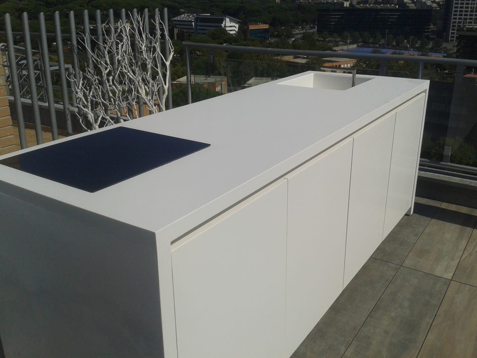 Isola bianca per cucina da esterno con piano cottura e lavello su un terrazzo.