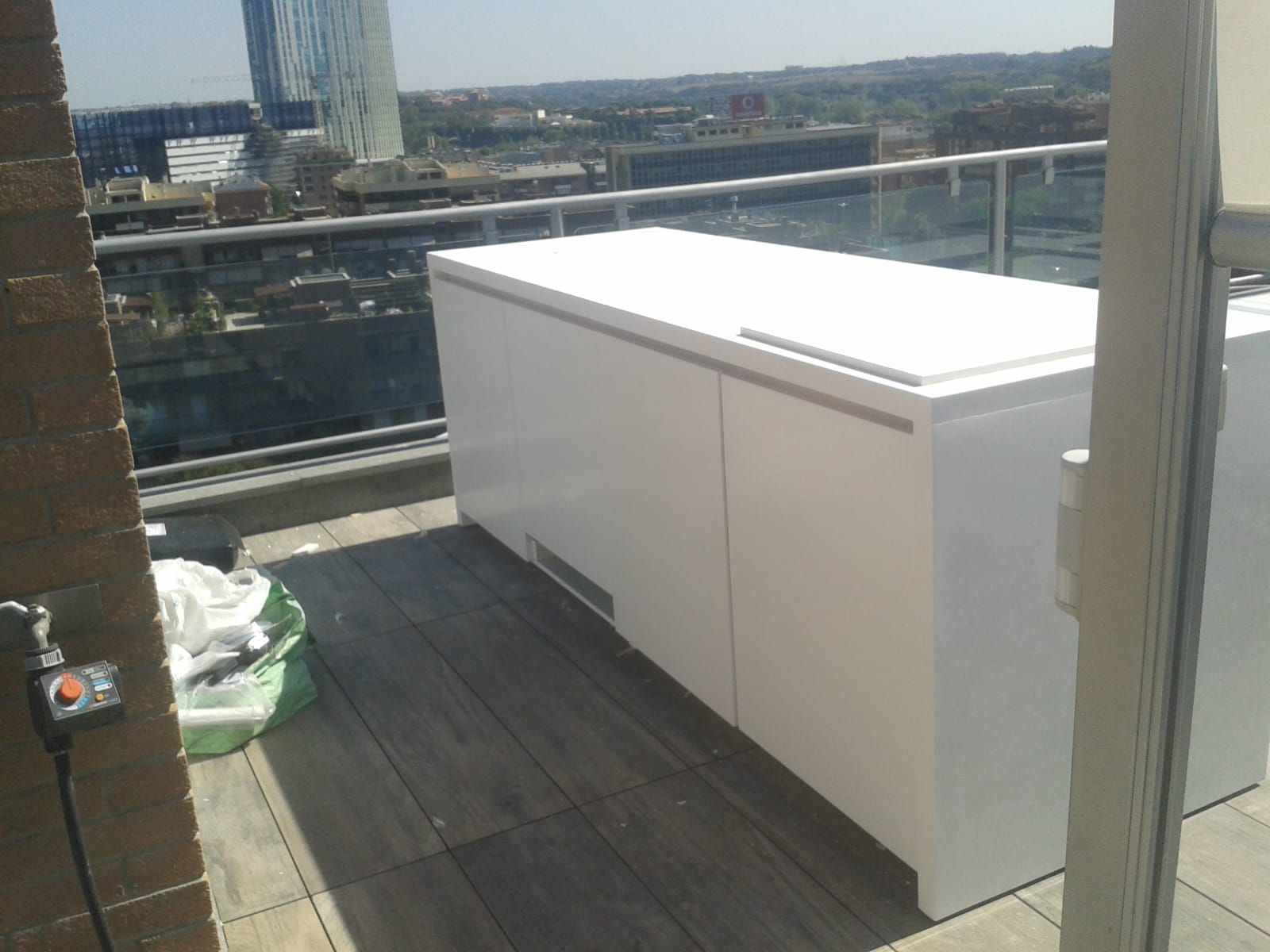 Congelatore bianco su una terrazza in legno, con vista sullo skyline della città. Giornata di sole.