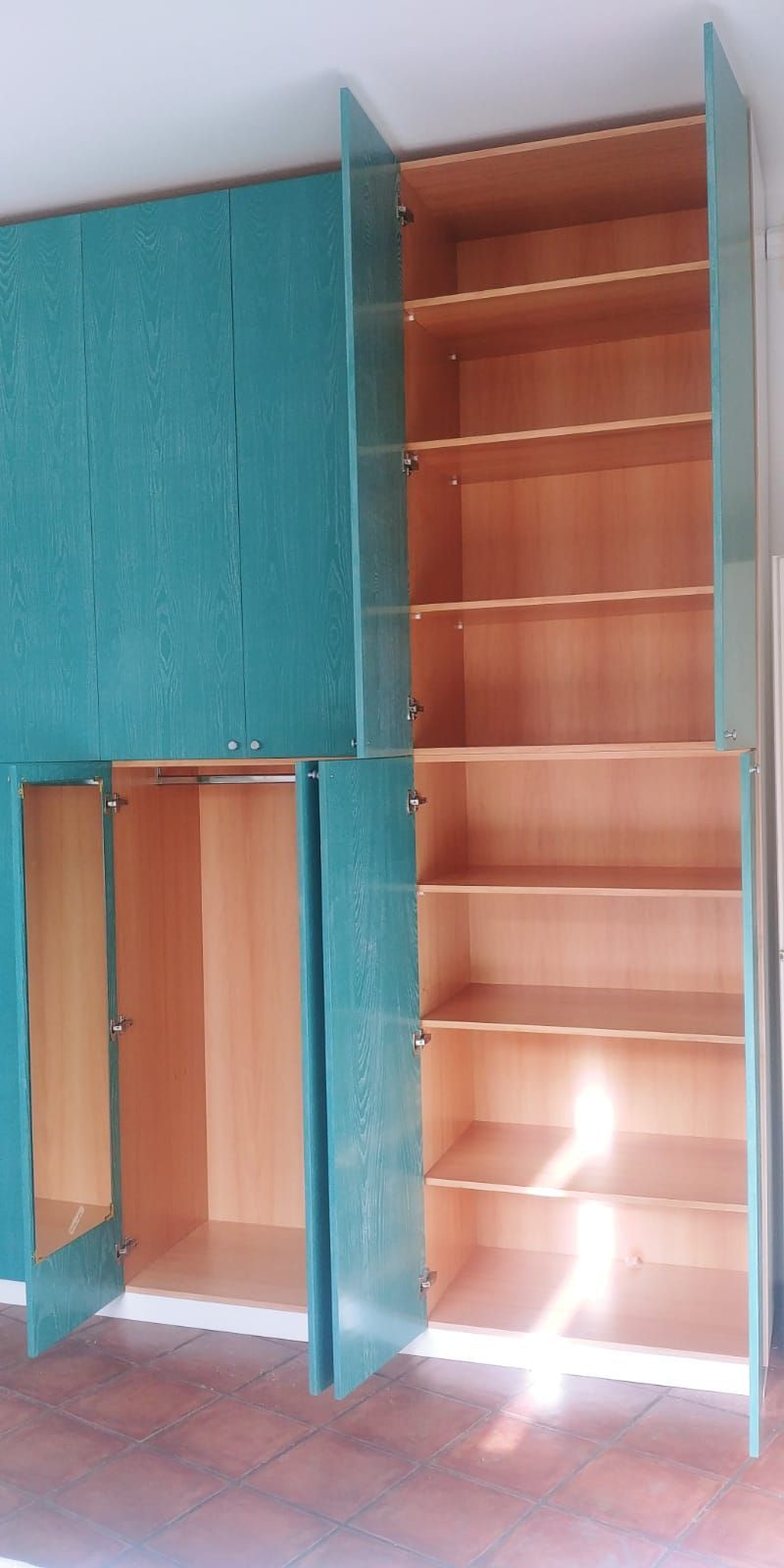 Armadietti contenitori color verde acqua con ante aperte, che rivelano ripiani in legno contro una parete di colore chiaro.