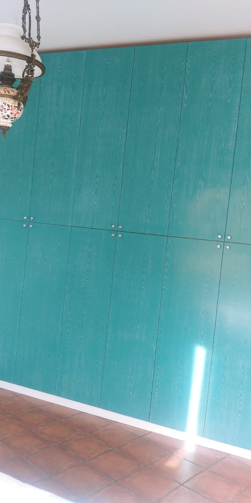 Parete color verde acqua con una luce verticale brillante e una lampada vintage appesa.