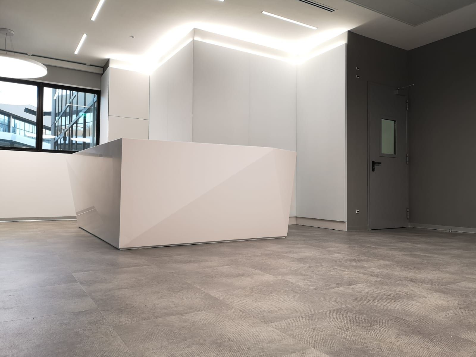 Reception bianca con elementi geometrici in un ufficio moderno. Pareti, pavimento e porta grigi.