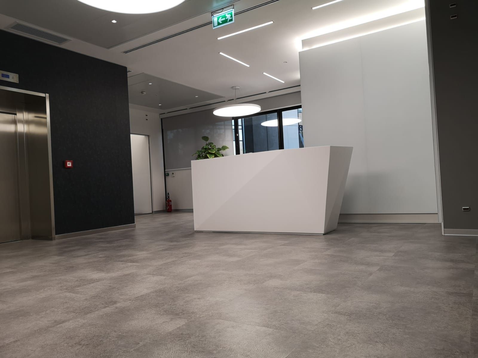 Moderna area reception per ufficio con bancone bianco, ascensore e pavimento grigio.