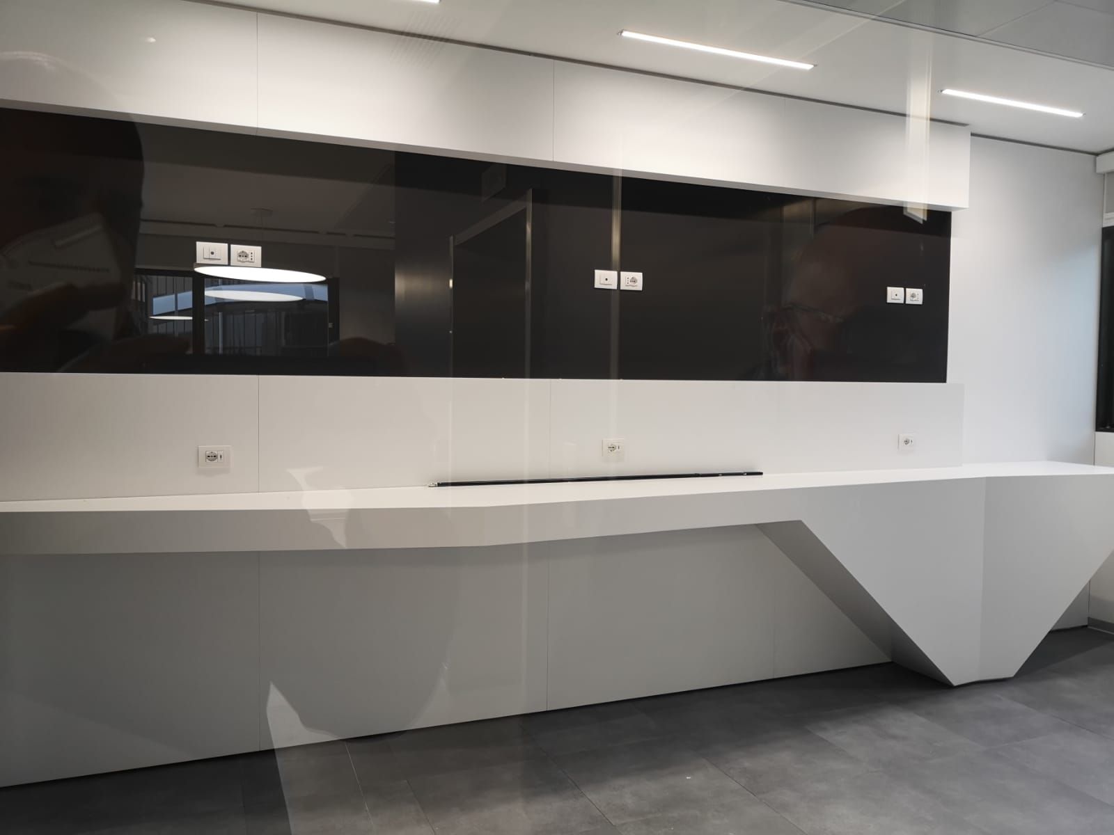 Moderno bancone bianco con design angolato, paraschizzi nero e illuminazione dall'alto all'interno di un edificio.
