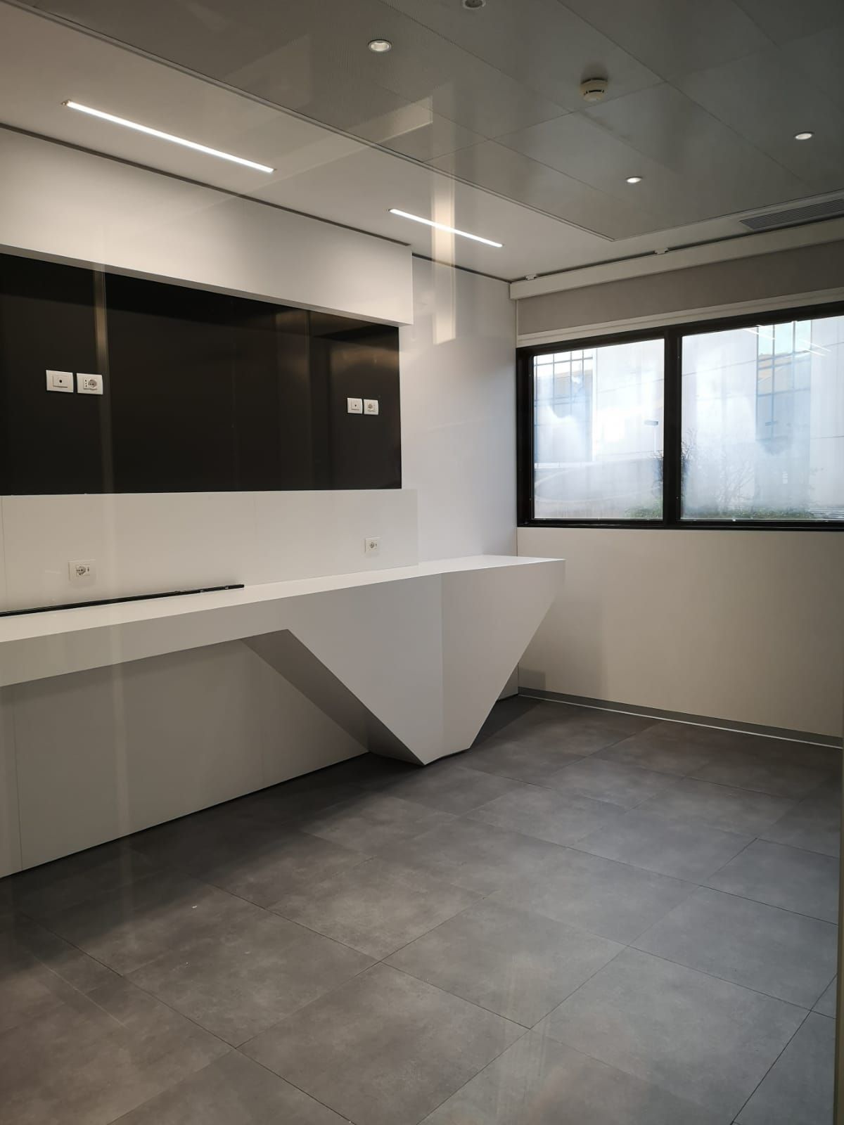 Moderno ufficio con scrivania angolare bianca, TV, pavimento grigio e finestra.