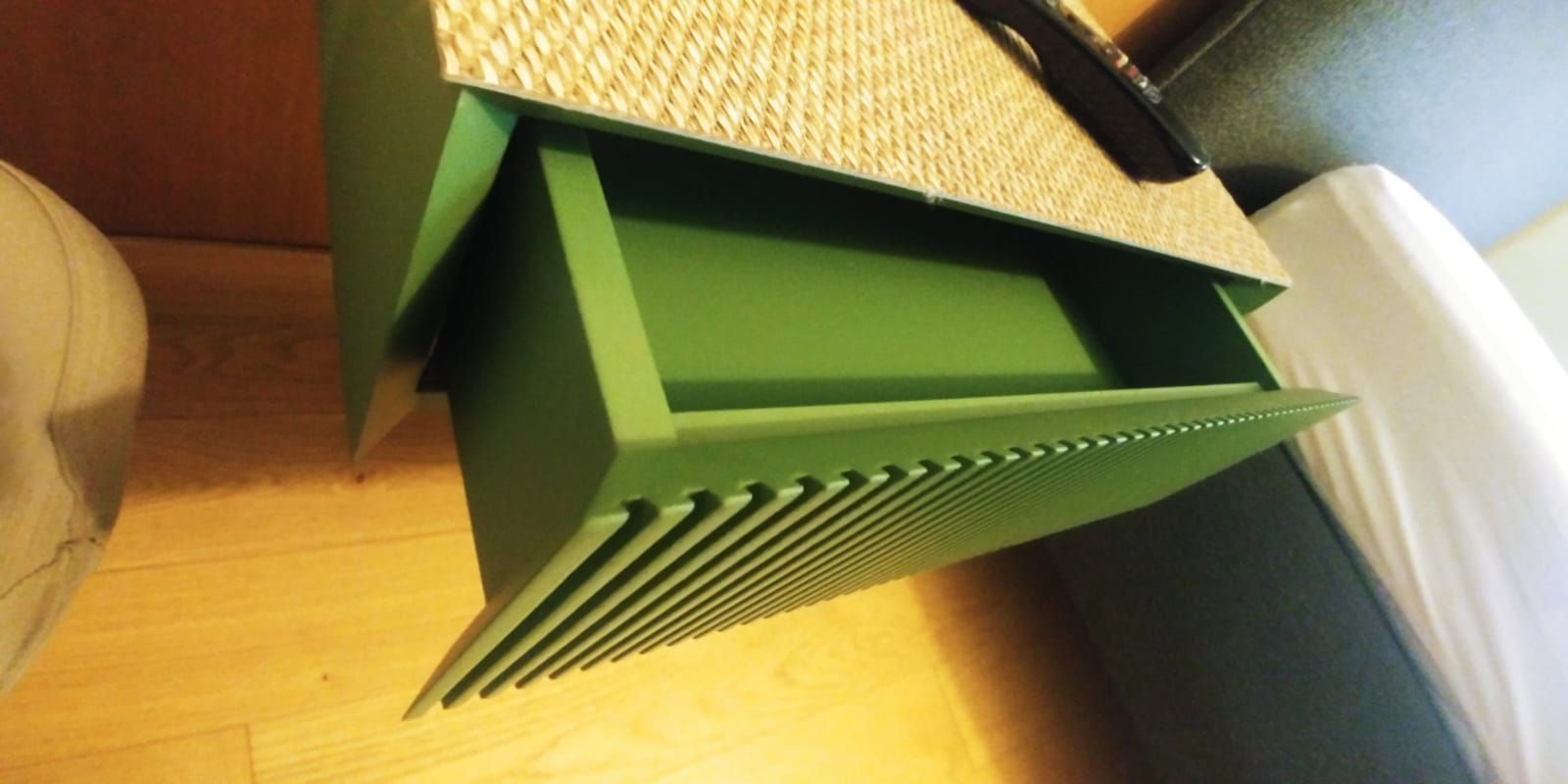 Cassetto verde con frontale decorativo e piano intrecciato, su un pavimento in legno.