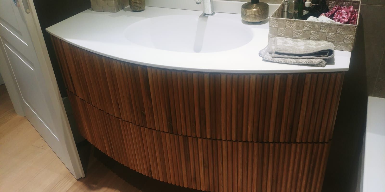 Mobile da bagno in legno curvato con piano bianco. Il lavabo è incassato nel piano.